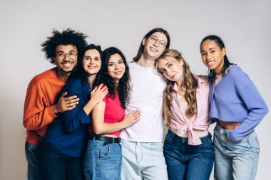 Diverse group of young adults smiling and hugging in bright studio, community and joy with casual clothing and relaxed, confident poses on white background. Friendship concept