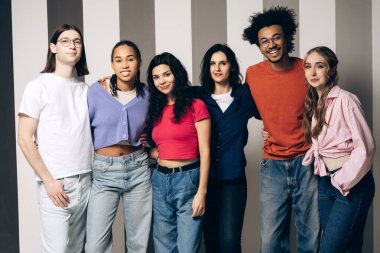 Diverse group of young multinational women and men standing together smiling looking at camera on striped background, promoting concepts of community, unity, and friendship