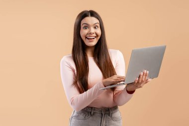 Genç bir kadın dizüstü bilgisayarında gördüğü bir şeye şaşırıp sevinçle tepki veriyor.