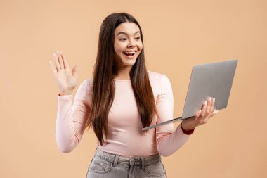 Mutlu genç bir kadın video görüşmesinde elini sallıyor ve ekranda gülümsüyor.