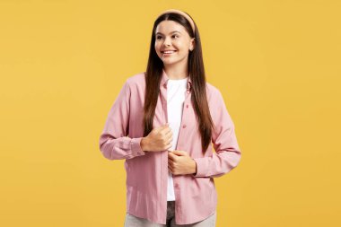 Genç esmer kadın neşeyle gülümsüyor, açık pembe gömlekli sarı arka planda duruyor.