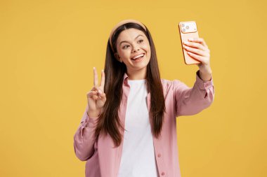 Mutlu kadın sarı arka planda kendini çekerken zafer jesti yapıyor.