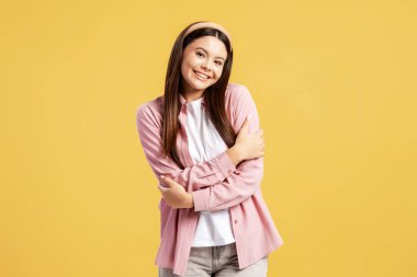 Kendini kucaklayan mutlu genç bir kadın, sarı arka planda kendine güvenini ve sevgisini hissediyor.