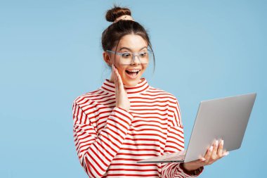 Beklenmedik iyi haberler gören heyecanlı genç bir kadın ve dizüstü bilgisayarında şaşkınlıkla tepki veriyor.