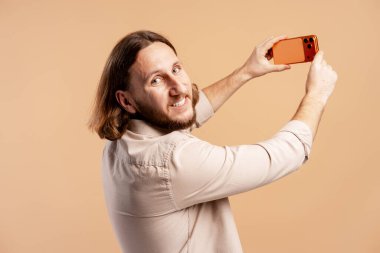 Gülümseyen bir adam, arka planda cep telefonuyla kendi portresini çekiyor.