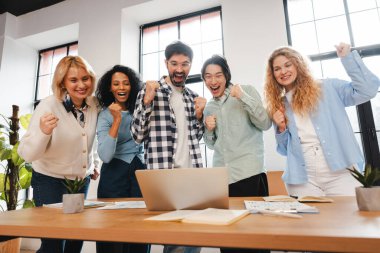 Muhtelif çalışma ekipleri ofiste bir dizüstü bilgisayara bakarken başarıyı coşkuyla ve neşeyle kutluyorlar.