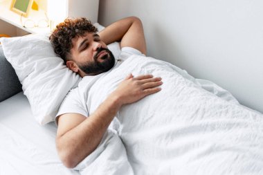 Yatakta uyuyan genç adam gözleri kapalı, elleri göğsünde dinleniyor, dinleniyor.