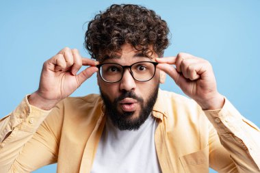 İfadesini değiştiren, bardaklarını kaldıran, açık mavi arka plana şaşıran bir adam.