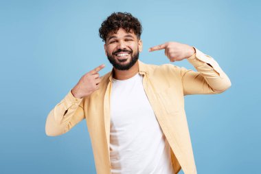 Kıvırcık saçlı gülümseyen adam temiz dişlerini gösteriyor, diş sağlığı ve ağız sağlığını destekliyor.