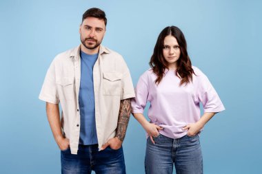 Genç adam ve kadın ayakta duruyor, kameraya ciddi ciddi bakıyor, özgüven ve kararlılık gösteriyor.