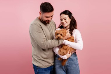 Sevimli bir köpeği kucaklayan ve okşayan genç çift, aile sevgisini ve evcil hayvan sahipliğini sembolize ediyor.