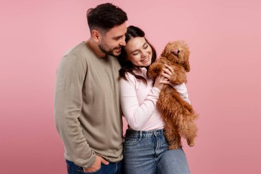 Sevimli bir kaniş köpeğini kucaklayan mutlu genç çift, sevgi ve aile bağlarını gösteriyor.