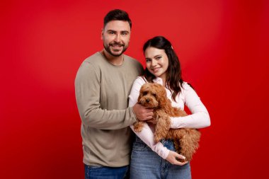 Sevdikleri hayvanı ellerinde tutan mutlu çift, kırmızı bir arka planda aşkı ve arkadaşlığı kutluyorlar.