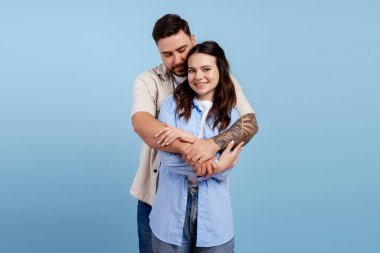 Mutlu çift kucaklaşır, samimiyet ve beraberlik gösterir açık mavi bir arka planda.