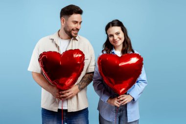 Kalp şeklinde balonlar tutan genç adam ve kadın, aşkı simgeliyor ve Sevgililer Günü 'nü kutluyorlar.