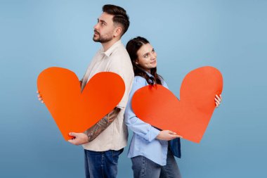 Sevgililer Günü 'nü kutlayan kırmızı kalpli genç çift mavi arka planda duruyor.