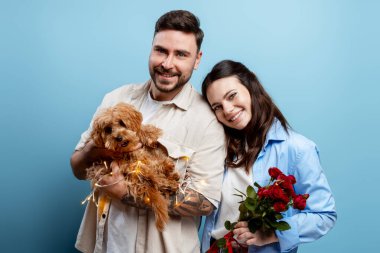 Köpekleri ve kırmızı gülleri kucaklayan neşeli genç çift aşkı ve ilişkileri kutluyorlar.