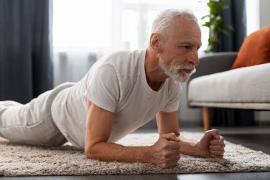 Üst düzey bir adam zeminde kalas egzersizi yapıyor. Ev ortamında çekirdek dayanıklılık kazanıyor.