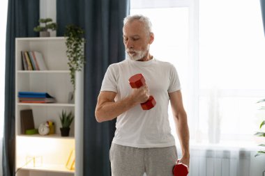 Son sınıf öğrencisi oturma odasında kırmızı halterlerle çalışıyor. Sağlıklı bir yaşam tarzına odaklanıyor.