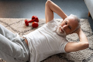 Son sınıf öğrencisi halının üzerinde uzanıyor, spor yaparken mekik çekiyor.