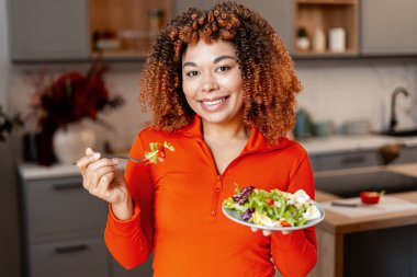 Taze salata yerken gülümseyen, sağlıklı beslenmeyi kucaklayan ve dengeli bir yaşam tarzı olan bir kadın.
