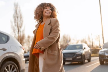 Genç bir kadın otoparkta yürürken gülümsüyor, altın saatin tadını çıkarıyor.