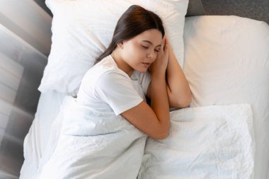 Beyaz çarşaflarda uyuyan genç bir kadın, yatak odasında huzur ve huzur dolu rüyalar görüyor.