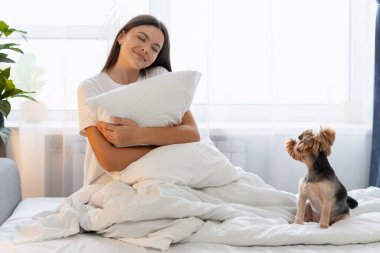 Genç bir kadın yastığa sarılıyor, sabah rahatlığının tadını çıkarıyor.