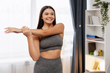 Mutlu genç bir kadın modern oturma odasında ısınma egzersizi yapıyor.