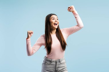 Gündelik giysiler giymiş genç bir kız başarıyı kollarını kaldırarak kutluyor mavi arka planda soyutlanmış bir şekilde başka yere bakıyor. Zafer konsepti