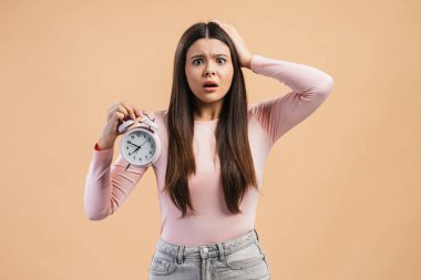 Acil durum ve panik halinde olan üzgün genç kız bej arka planda izole edilmiş kamera görüntülerine bakıyor. Son teslim tarihi kavramı