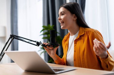 Genç bir kadın mikrofona konuşuyor, online yayın için bir podcast kaydediyor.