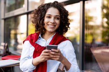 Cep telefonu kullanan, cep telefonu kullanan, kafede oturup sohbet eden, gülümseyen güzel bir kadın. Sosyal medya kavramı