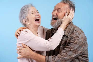 Kıdemli çift sarılıyor ve yüksek sesle gülüyor, mavi bir arka planda mutluluğu kutluyorlar.