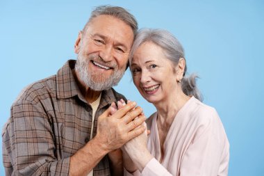 Kıdemli çift kameraya gülümsüyor, canlı mavi bir arka planda el ele tutuşuyorlar, aşkı ve birlikteliği ifade ediyorlar.