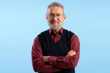 Kendine güvenen yaşlı bir adamın portresi. Gri saçlı ve sakallı. Mavi arka planda poz veriyor.