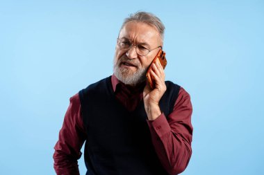 Kıdemli adam konuşuyor, şaşırmış ve kafası karışmış bir ifadeyle cep telefonuyla konuşuyor.