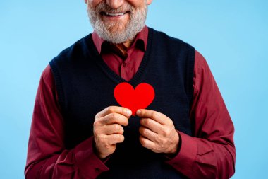 Kıdemli adam gülümsüyor, elinde kırmızı bir kalp taşıyor, aşkı, sağlığı ve hayırseverliği temsil ediyor.