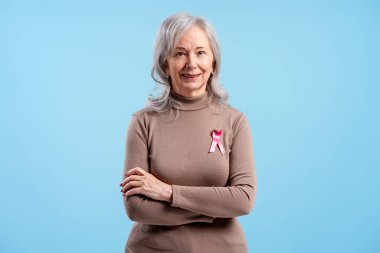 Göğüs kanserini destekleyen gülümseyen bir kadın, mavi arka planda pembe bir kurdele takıyor.