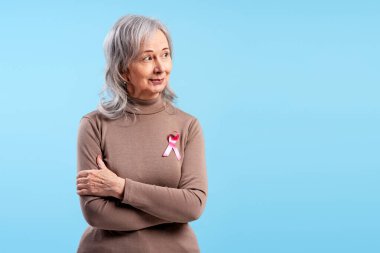 Son sınıf öğrencisi kadın göğüs kanseri farkındalığını gururla destekliyor. Pembe kurdelesiyle umut dolu görünüyor.