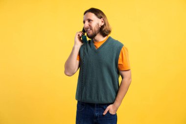Gülümseyen bir adam, açık sarı arka plandaki bir konuşma için klasik bir telefon kullanıyor.