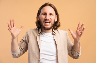 Genç adam heyecanlı ve şaşırmış hissediyor, bej arka planda açık bir ağızla el ele tutuşuyor.