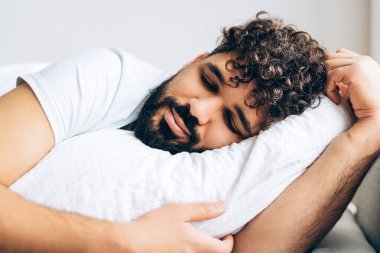 Genç yakışıklı adam yatakta yumuşak yastıkta huzur içinde uyuyor. Rahatlatıcı kavram