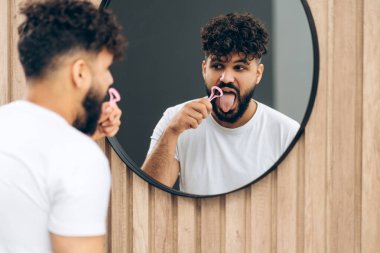 Genç adam evdeki tuvalette ağız temizliği için dil kazıyıcı kullanıyor. Kişisel bakım, diş konsepti