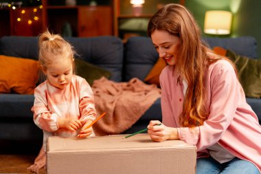 Anne ve kızı yaratıcı oyun zamanlarından zevk alıyorlar, oturma odalarındaki karton kutunun üzerine resim çiziyorlar.