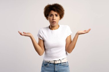 Kafası karışmış, omuz silkmiş, beyaz arka planda izole kameraya bakarken belirsizlik gösteren üzgün bir kadın. Sorun kavramı