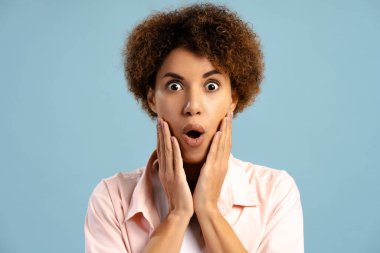 Mavi arka planda izole edilmiş kameraya bakarken şaşırmış genç bir kadının portresi. İyi haber konsepti