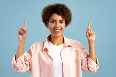 Mavi arka planda izole edilmiş reklam alanı gösteren mutlu Afrikalı Amerikalı kadın. Alışveriş konsepti