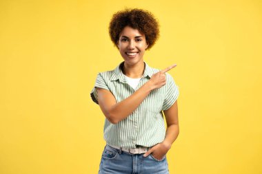 Mutlu gülümseyen Afrikalı Amerikalı kadın sarı arka planda izole edilmiş fotokopi alanını işaret ediyor. Kameraya bakan neşeli kadın pozu. Reklam kavramı