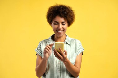 Gülümseyen Afro-Amerikan kadın sarı arka planda akıllı telefon mesajı kullanıyor. Olumlu kadın sohbeti. Sosyal medya kavramı
